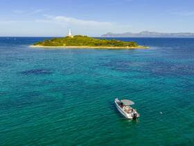 A scenic view of a boat anchored near a picturesque island with a lighthouse, showcasing the beauty of coastal adventures.