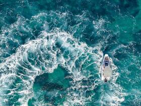 Aerial view of a boat navigating through vibrant turquoise waters, showcasing the beauty of the ocean and the vessel's sleek design.