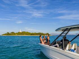 A group of friends enjoys a sunny day on a boat near a picturesque island with a lighthouse, perfect for fun and relaxation on the water.