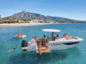 A lively group enjoys a day on the water, with some swimming and others relaxing on a pontoon boat near the beach — perfect for summer fun and social gatherings.