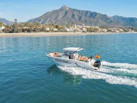 A lively group enjoys a day on the water aboard a boat in Marbella, with stunning mountain views and a beautiful beach backdrop.