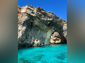 A stunning view of a rocky coastline with a natural arch, surrounded by crystal-clear turquoise waters — a perfect destination for boat tours and scenic exploration.