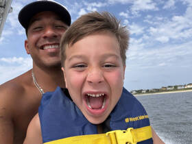 A joyful moment captured on a boat with a smiling adult and a child wearing life jackets, showcasing the excitement of family fun on the water.
