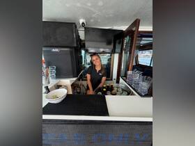 A friendly bartender smiles from behind the bar on a boat, ready to serve refreshing cocktails and drinks to guests enjoying their time on the water.