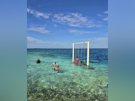 A lively group enjoys a fun day at the beach, playing in the crystal-clear waters and swinging from a unique ocean swing — perfect for memorable summer adventures.