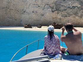 A couple enjoys the stunning view of a shipwreck on a secluded beach, capturing the moment from their boat — a perfect blend of adventure and scenic beauty.