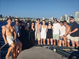 A lively group of friends enjoys a sunny day on the water, celebrating together aboard a boat with a stunning city backdrop.