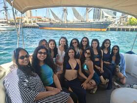 A lively group of friends enjoys a fun day on the water, celebrating together on a boat with the iconic Star of India in the background.