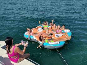 A lively group of friends enjoys a fun day on the water, relaxing on a floating mat with drinks in hand — perfect for summer parties and celebrations.