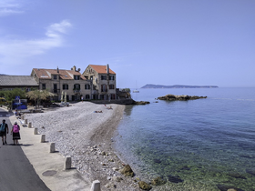 A picturesque view of a serene beach with people strolling along the shore, showcasing beautiful coastal scenery and nearby islands.