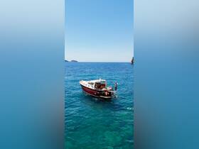 A person joyfully poses on the deck of a boat in crystal-clear waters, showcasing the perfect setting for summer adventures and water activities.