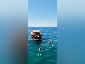 A lively group enjoys a refreshing swim in crystal-clear waters while a boat is anchored nearby, perfect for summer fun and aquatic adventures.