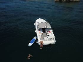 Aerial view of a boat with guests enjoying the water, one person swimming and another relaxing on the deck — a perfect scene for summer fun and water activities.