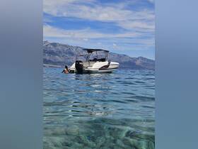 A person enjoys swimming near a sleek boat in crystal-clear waters, with stunning mountain scenery in the background — a perfect summer getaway.