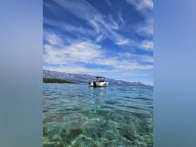 A person enjoys a refreshing swim in crystal-clear waters near a boat, with stunning mountain scenery in the background — a perfect snapshot of a summer day on the water.
