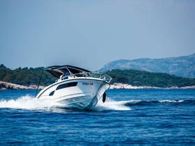 A sleek speedboat navigates through clear waters, showcasing its dynamic design and performance against a scenic backdrop of lush hills.