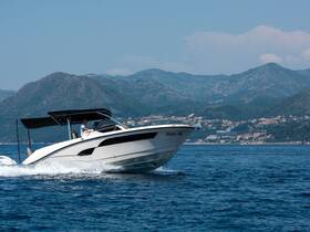 A sleek speedboat glides through the water with a driver at the helm, showcasing its elegant design against a backdrop of mountains.