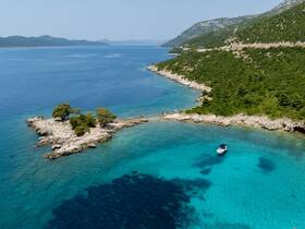 Aerial view of a boat cruising in crystal-clear turquoise waters, surrounded by lush greenery and rocky shores — a perfect scene for exploring hidden coves.