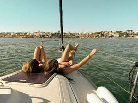 Two friends relax on the deck of a sailboat, enjoying the sun and scenic views — a perfect moment for a sailing adventure.