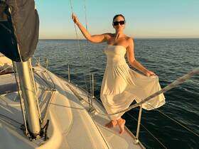 A woman poses gracefully on the deck of a sailboat, enjoying the serene ocean view during sunset — a perfect moment for sailing enthusiasts.