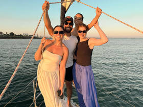 A joyful group poses on the bow of a sailboat during sunset, capturing the essence of a perfect sailing adventure with friends.