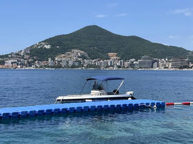 A sleek speedboat is docked near a scenic coastal town, surrounded by clear waters and lush hills, perfect for a day of relaxation on the water.