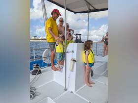 A family enjoys a sailing experience on a boat, with children wearing life jackets and adults engaging at the helm — a perfect day on the water.