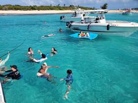 A lively group enjoys a fun day in the turquoise waters, swimming and relaxing around a boat — perfect for beach parties and family outings.