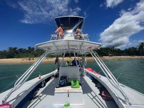 Guests enjoy a sunny day on a boat with a beautiful beach backdrop, perfect for a fun day out on the water.