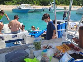 A lively group enjoys a fun day on the water, with kids swimming and adults relaxing on the boat, surrounded by delicious snacks and drinks.