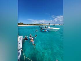 A lively group enjoys a fun day in the turquoise waters, swimming and relaxing around a pontoon boat at a picturesque sandbar — perfect for summer adventures.