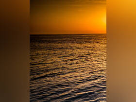 A serene sunset over the ocean, creating a beautiful golden reflection on the water's surface.