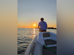 A serene sunset view from the bow of a boat, with a person enjoying the tranquil waters — perfect for romantic evenings or peaceful getaways.