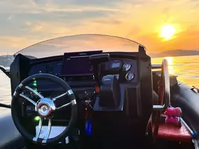 A stunning view of the helm of a boat during sunset, showcasing the console and steering wheel, with a hint of a passenger relaxing in the background.