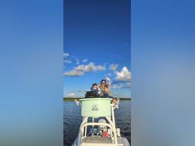 Two children enjoy a fun moment on a boat, waving at the camera against a backdrop of blue skies and fluffy clouds — a perfect snapshot of a joyful day on the water.