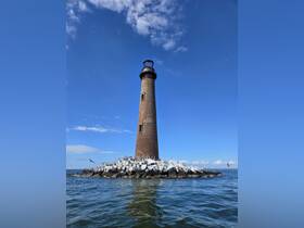 A scenic view of a lighthouse surrounded by water, showcasing the structure against a clear blue sky. Ideal for maritime photography enthusiasts.