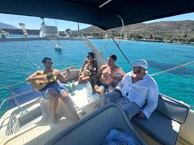 A lively group enjoys a sunny day on the boat, with one member playing guitar while others relax and celebrate — perfect for a memorable day on the water.