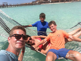 A joyful family enjoys a relaxing moment in a hammock by the beach, surrounded by clear turquoise waters — perfect for creating unforgettable vacation memories.