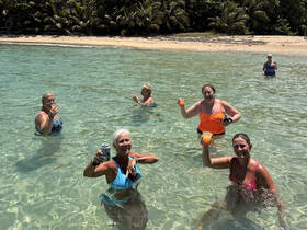 A lively group of friends enjoys refreshing cocktails while wading in crystal-clear waters, celebrating their beach day in paradise.