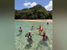 A joyful group of women enjoys a refreshing swim in crystal-clear waters while sipping cocktails, creating unforgettable beach memories.