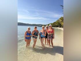 A joyful group of women enjoys a sunny day at the beach, celebrating together in the shallow waters — perfect for memorable moments and fun in the sun.