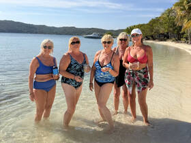 A lively group of friends enjoys a day at the beach, wading in the shallow water and celebrating with drinks — perfect for a fun getaway.