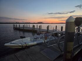 A sleek speedboat is docked at a pier during a stunning sunset, showcasing the tranquil beauty of evening waters.