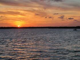 A stunning sunset over tranquil waters, with a silhouette of a boat in the distance, creating a picturesque scene perfect for evening cruises.