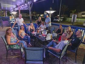 A lively group gathers around a table enjoying drinks and conversation in a vibrant outdoor setting, perfect for socializing and celebrations.