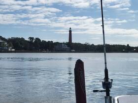 A serene view of a lighthouse along the water, with a fishing rod in the foreground, capturing the essence of a peaceful day on the water.
