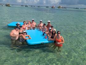 A lively group enjoys drinks and fun on a floating mat in shallow waters, perfect for a day of relaxation and celebration on the water.