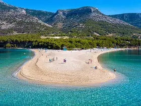 A stunning aerial view of a picturesque beach with visitors enjoying the sun and clear waters, perfect for a relaxing day by the coast.