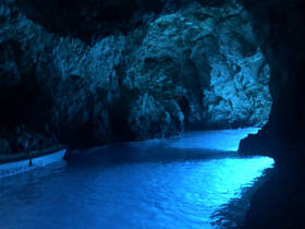 A stunning view of a boat navigating through a luminous cave, showcasing the vibrant blue waters and rocky formations — an unforgettable adventure in nature.