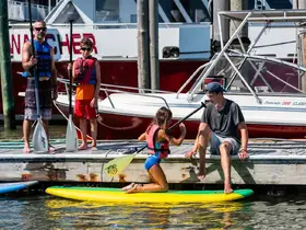 A family enjoys a sunny day at the dock, with kids paddleboarding and preparing for water activities — a perfect summer outing.